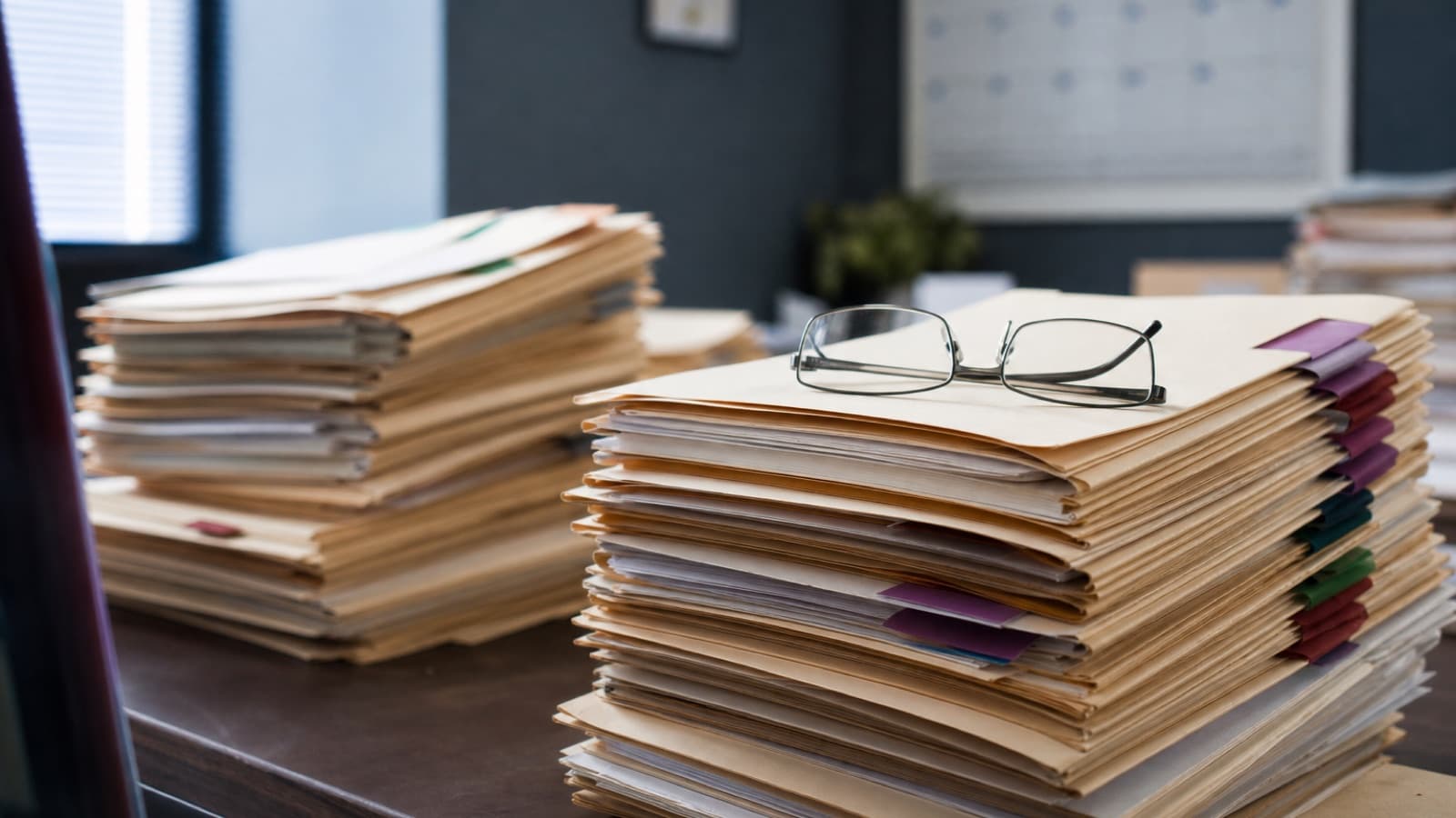 Stacks of tabbed medical record folders piled on a government office desk, representing CMS RADV audits expanding to 550+ MA plans
